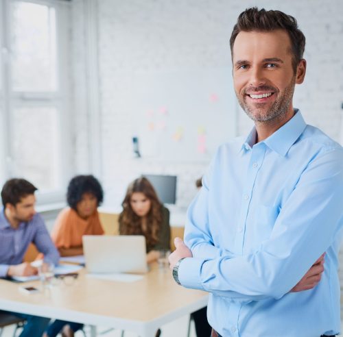 Portrait of cheerful business man standing in modern creative office with employees in background